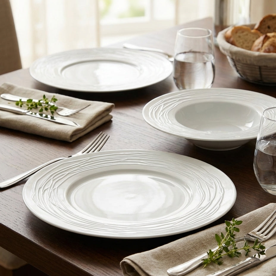 Dining table setting with white plates, silverware, and bread on a wooden table.
