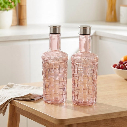 Two pink glass bottles with silver lids on a wooden table in a kitchen setting.