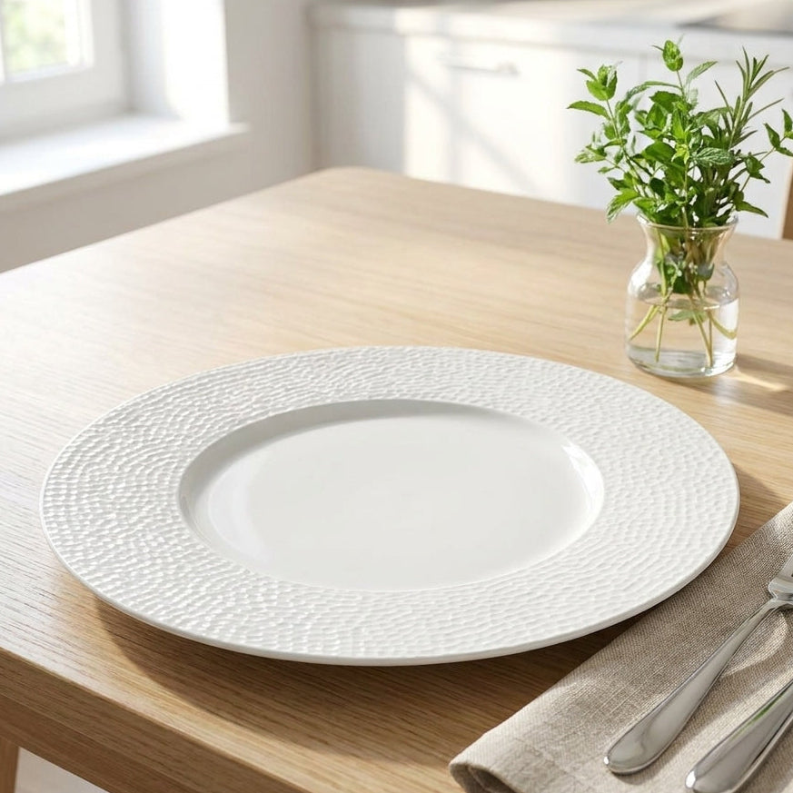 White textured plate on a wooden table with silverware and a plant