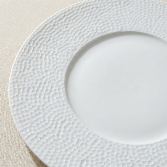 White ceramic plate with textured rim on a beige surface