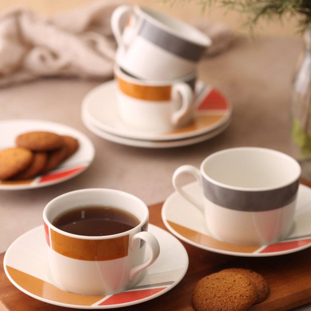 A set of white porcelain tea cups with orange and gray stripes on them, accompanied by saucers and cookies on a wooden surface.