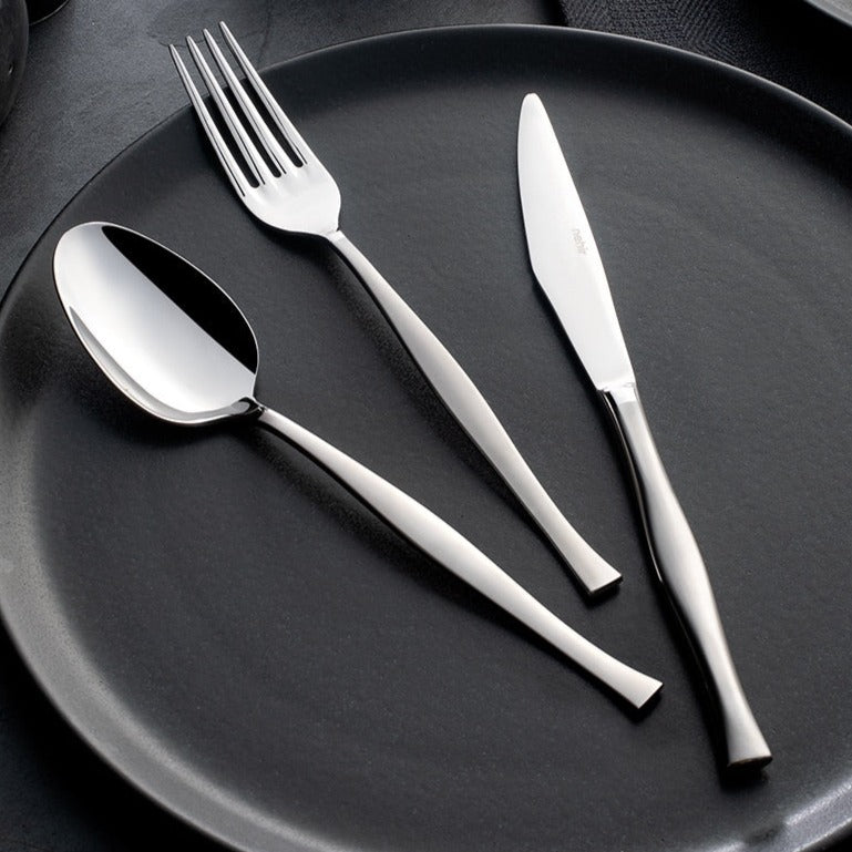 A set of silver cutlery including a soup ladle, service spoon, service fork, and a knife and fork set displayed on a dark plate.