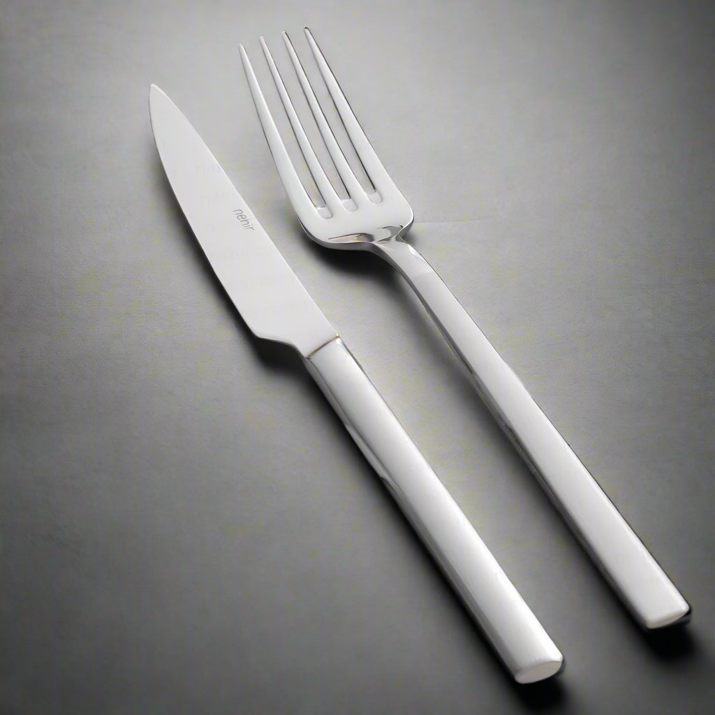 A set of silver cutlery, including a table spoon, table fork, and table knife, placed on a grey napkin with a sprig of thyme beside them.