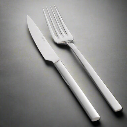 A set of silver cutlery, including a table spoon, table fork, and table knife, placed on a grey napkin with a sprig of thyme beside them.