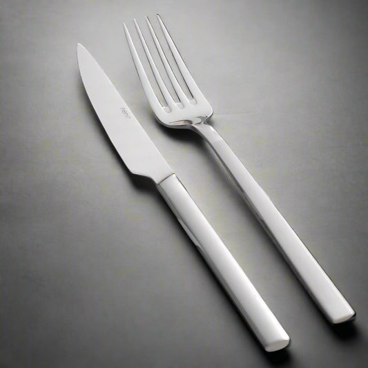 A set of silver cutlery, including a table spoon, table fork, and table knife, placed on a grey napkin with a sprig of thyme beside them.