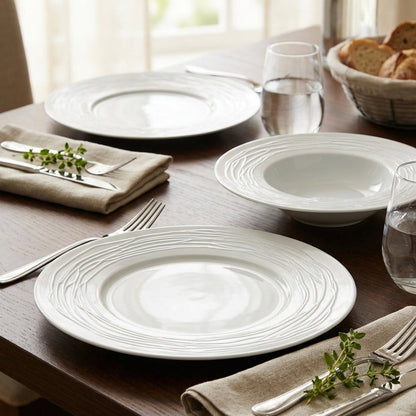 Dining table setting with white plates, silverware, and bread on a wooden table.
