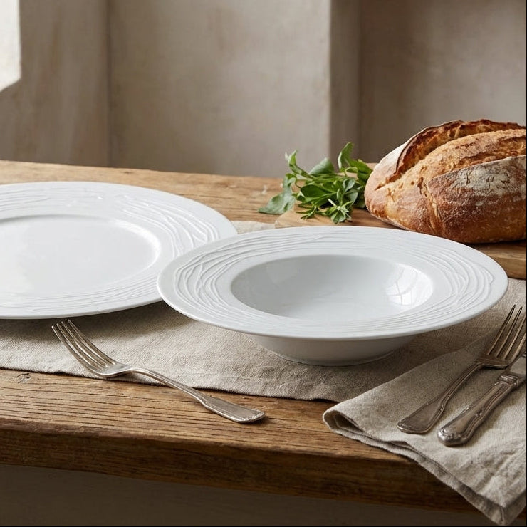 White ceramic plates and bowls on a wooden table with bread and olives.