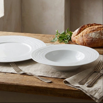 White ceramic plates and bowls on a wooden table with bread and olives.