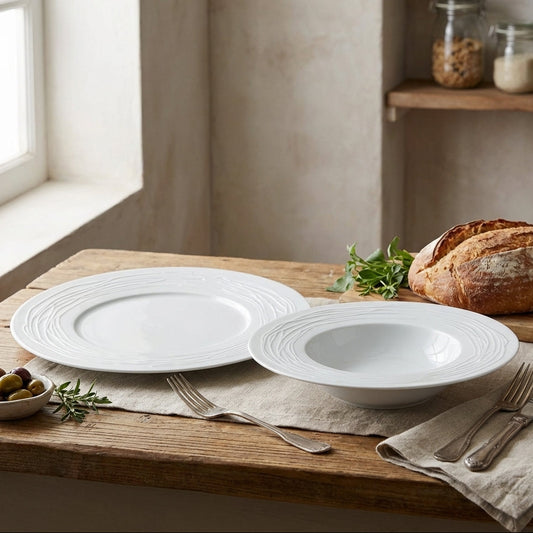 White ceramic plates and bowls on a wooden table with bread and olives.