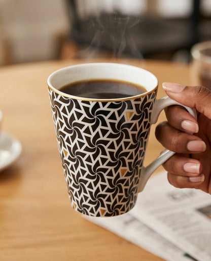 Person holding a patterned mug with steaming coffee on a wooden table.