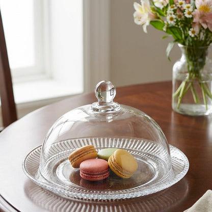 Glass cake stand with macarons on a wooden table, next to a vase of flowers.