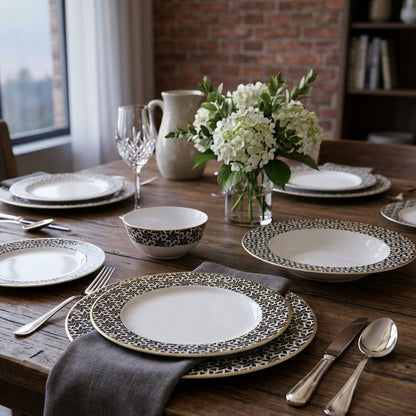 Dining table set with patterned plates, silverware, and a vase of flowers in a room with large windows.