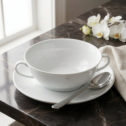 White ceramic bowl with saucer and spoon on a marble surface with flowers in the background