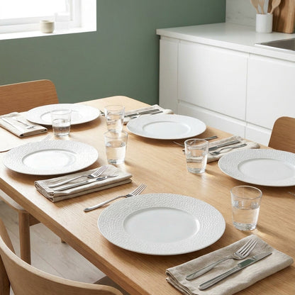 Dining table set with white plates, silverware, and glasses in a kitchen.