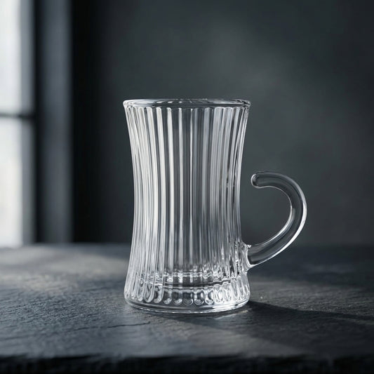 A clear ribbed glass mug with a curved handle, standing on a dark textured surface against a dark gray background.