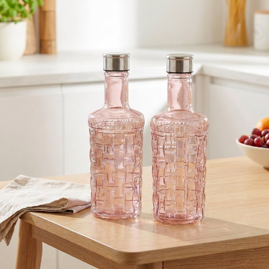 Two pink glass bottles with silver lids on a wooden table in a kitchen setting.