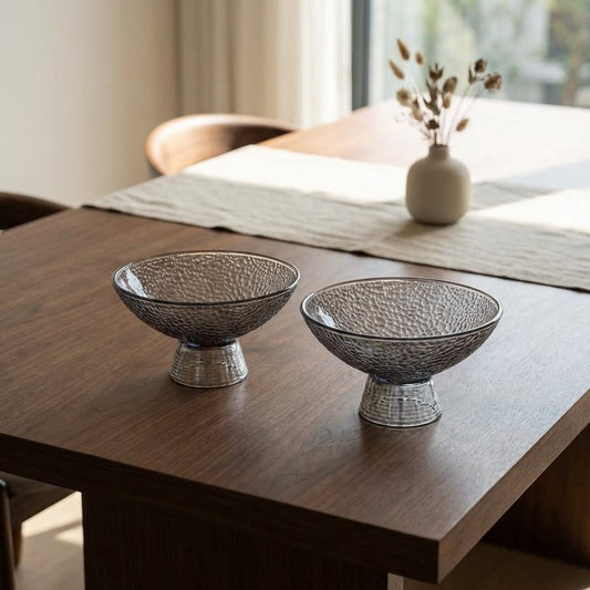 Two decorative bowls on a wooden table with a vase in the background.