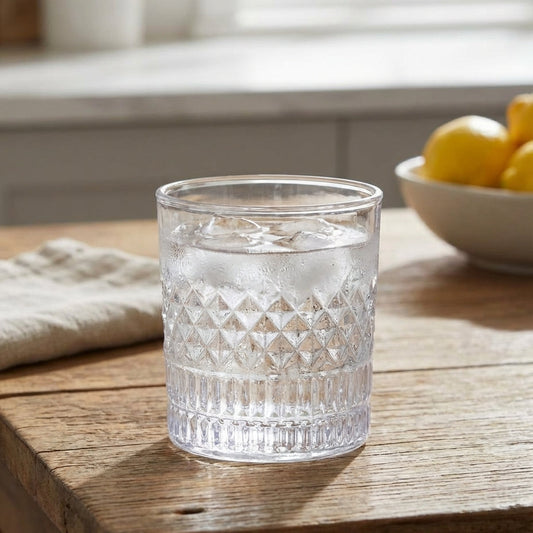 Clear glass with water on a wooden table with a bowl of lemons in the background