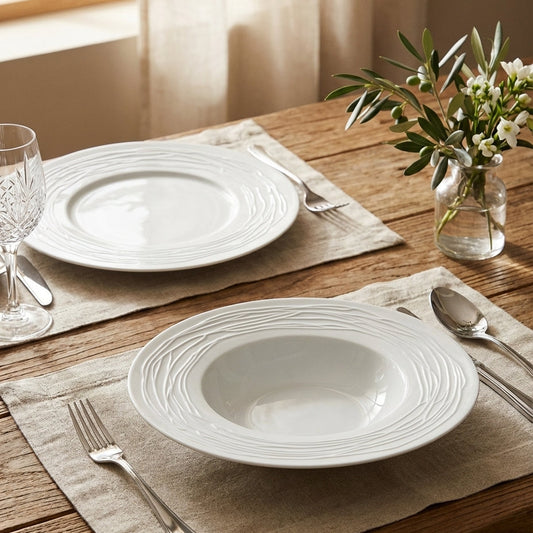 White ceramic plates on a wooden table with silverware and a vase of flowers.