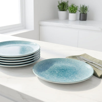 Set of blue ceramic plates on a white surface with green napkins and plants in the background.
