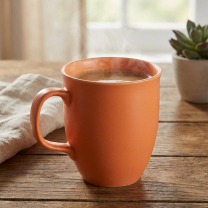 Orange mug with coffee on a wooden table with a window and plant in the background