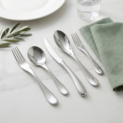 Silver cutlery set on a white surface with a green napkin and leaf decoration.