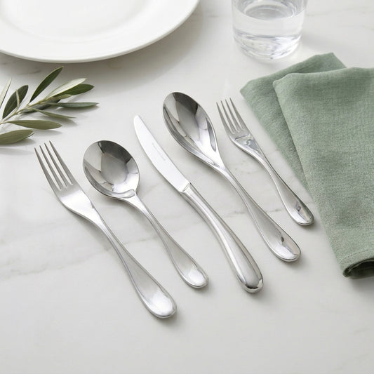 Silver cutlery set on a white surface with a green napkin and leaf decoration.