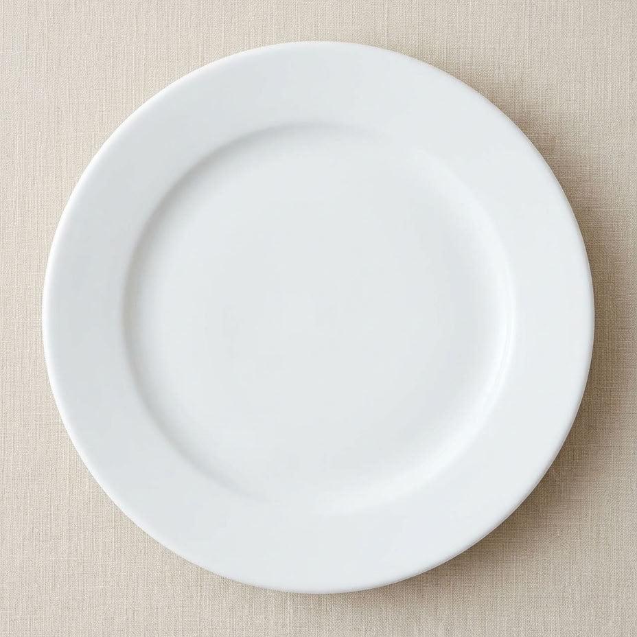A plain white ceramic plate photographed from above on a light beige textured fabric background.