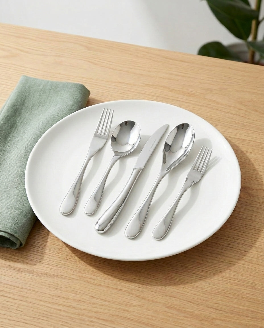 Set of silver cutlery on a white plate with a green napkin on a wooden surface.