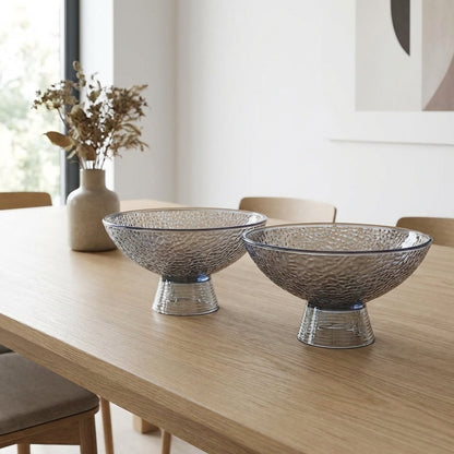 Two decorative glass bowls on a wooden table with a vase of dried flowers in the background.