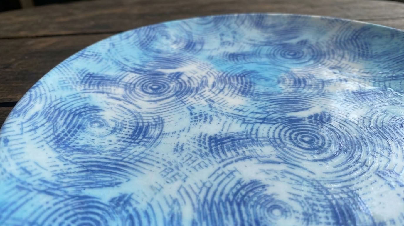 A close-up of a round ceramic plate with a blue and white swirling raindrop pattern, resting on a rustic wooden surface.