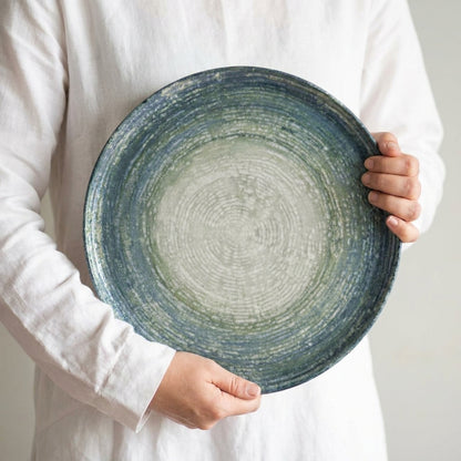 Person holding a blue ceramic plate with a textured surface