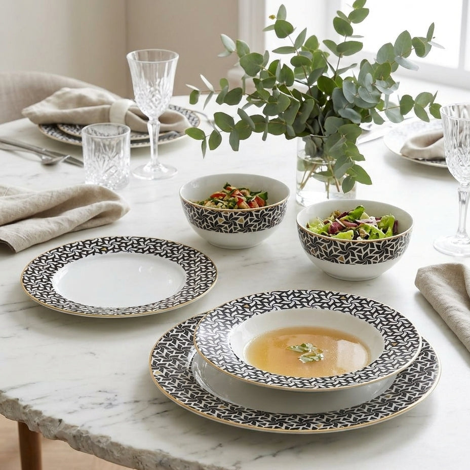 Dining table set with black and white patterned plates and bowls, featuring a vase of greenery.