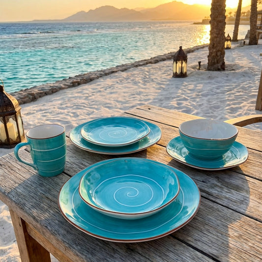 Turquoise ceramic tableware set on a wooden table by the beach at sunset.