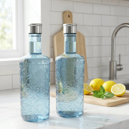 Two blue glass bottles with silver caps on a kitchen counter with lemons and mint leaves.