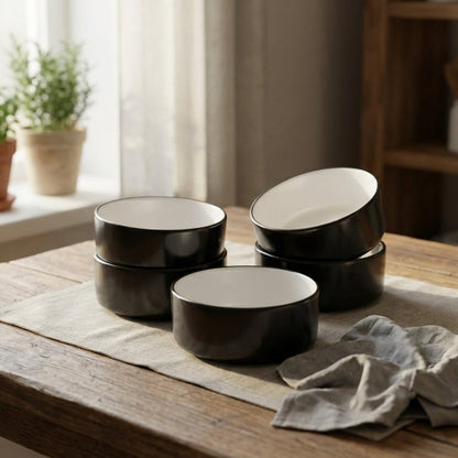 Set of black ceramic bowls on a wooden table with a neutral background