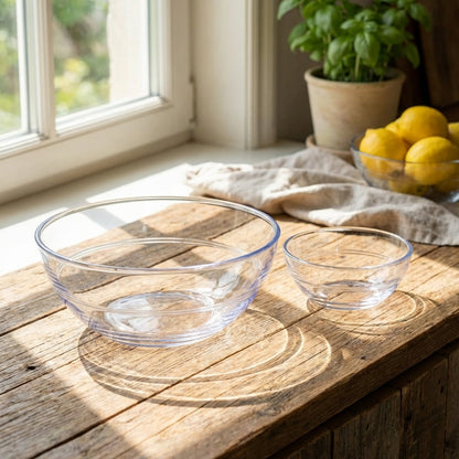 Clear glass bowls on a wooden surface with a window and plant in the background