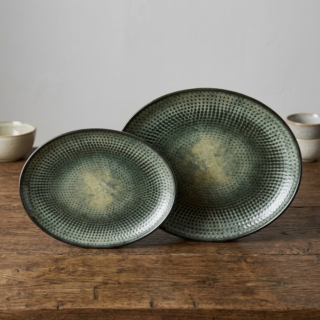 Two round ceramic serving platters with a textured, dimpled surface and a distressed olive green and beige glaze, displayed on a rustic wooden table.