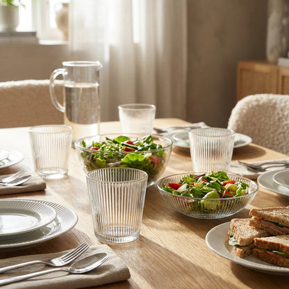 Dining table set with salad, sandwiches, and clear glasses in a bright room.