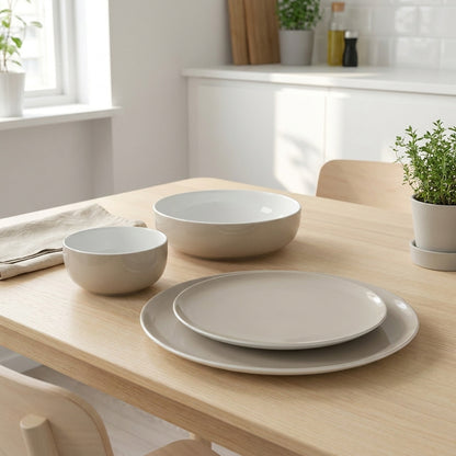 Set of light gray ceramic dishes on a wooden table in a bright kitchen.