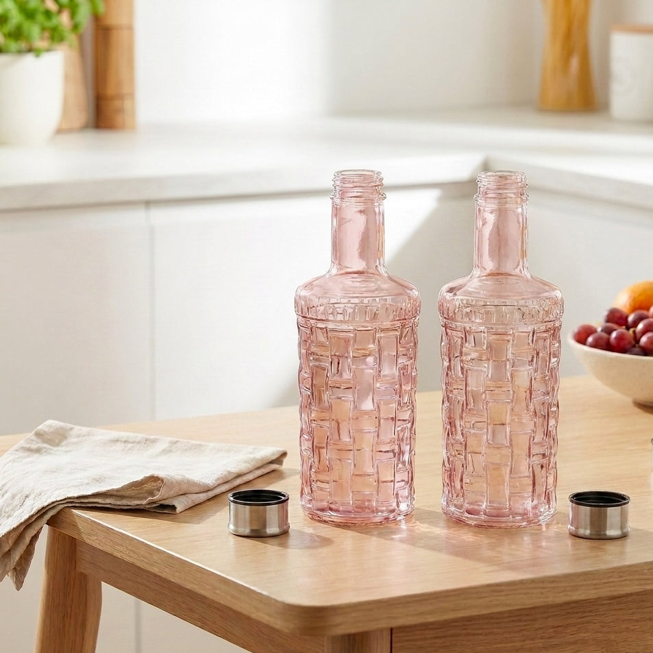 Two pink glass bottles on a wooden table with a kitchen background