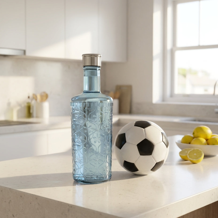 Clear glass bottle with silver cap on a kitchen counter with a soccer ball and lemons.