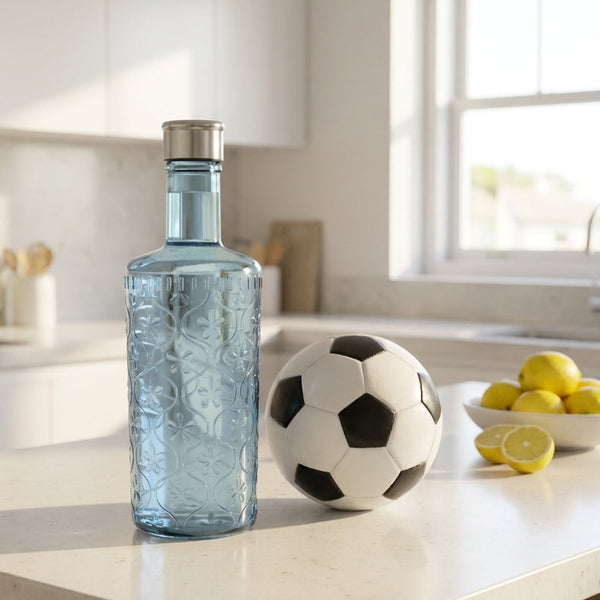 Clear glass bottle with silver cap on a kitchen counter with a soccer ball and lemons.