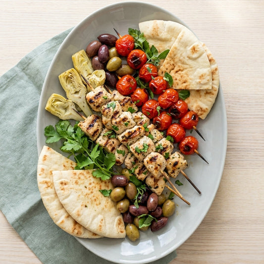 Platter of Greek-style skewers with pita bread, olives, and artichokes on a light surface.