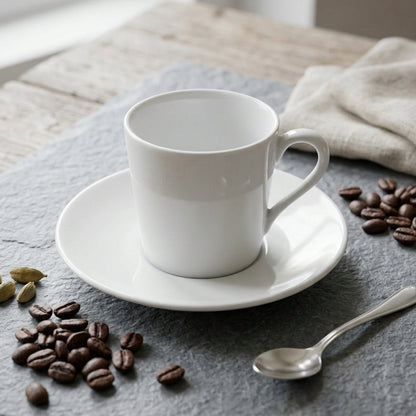White coffee cup on a saucer with coffee beans and a spoon on a gray surface.