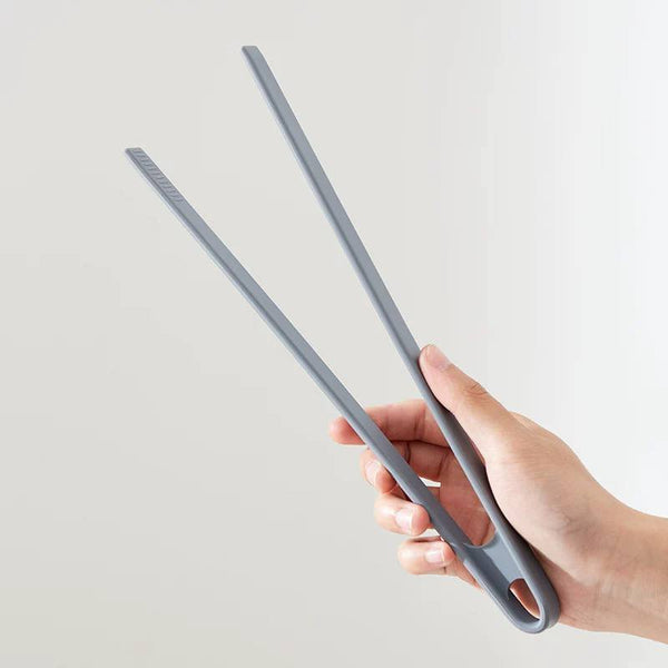 A pair of gray silicone food tongs being held by a hand against a light background.