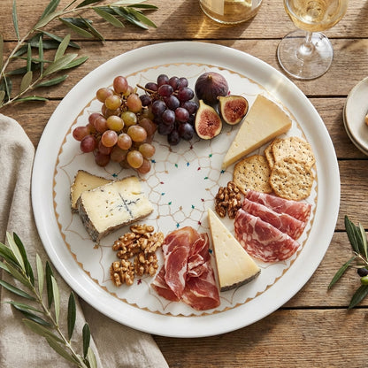 Platter of assorted meats, cheeses, and fruits on a wooden table with glasses of white wine.