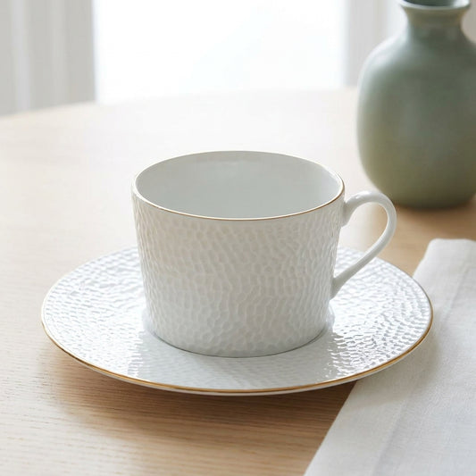 White textured teacup and saucer on a wooden surface with a light background