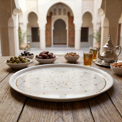 Tray with decorative patterns on a wooden table with olives, dates, and tea glasses in an outdoor setting.