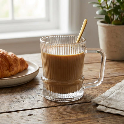 Clear glass mug with coffee and a croissant on a wooden table.
